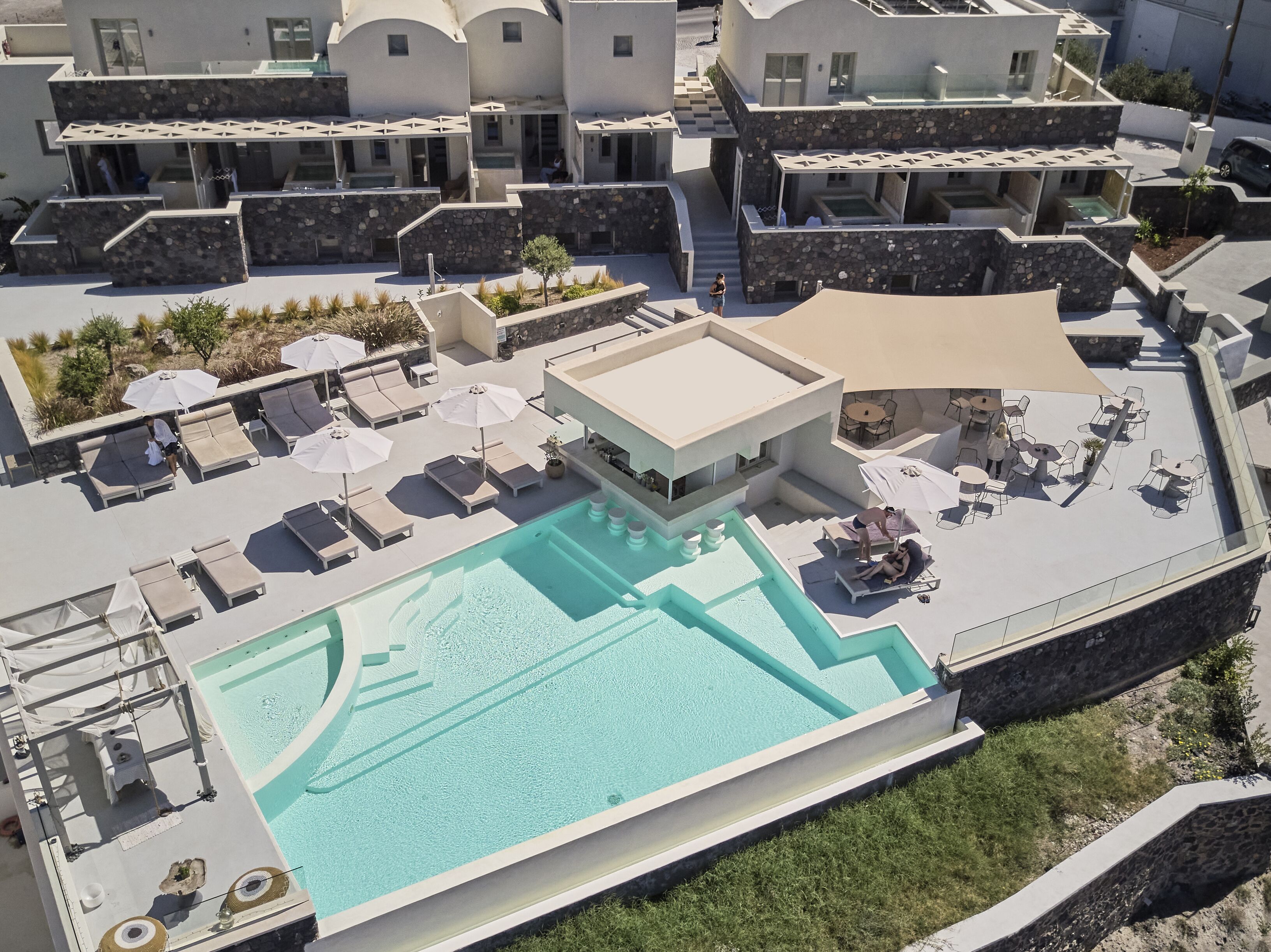 Un área de piscina en la azotea con sillones de descanso y sombrillas, rodeada de edificios modernos con fachadas de piedra.