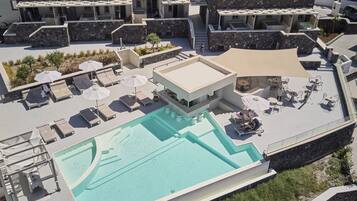 Un área de piscina en la azotea con sillones de descanso y sombrillas, rodeada de edificios modernos con fachadas de piedra.