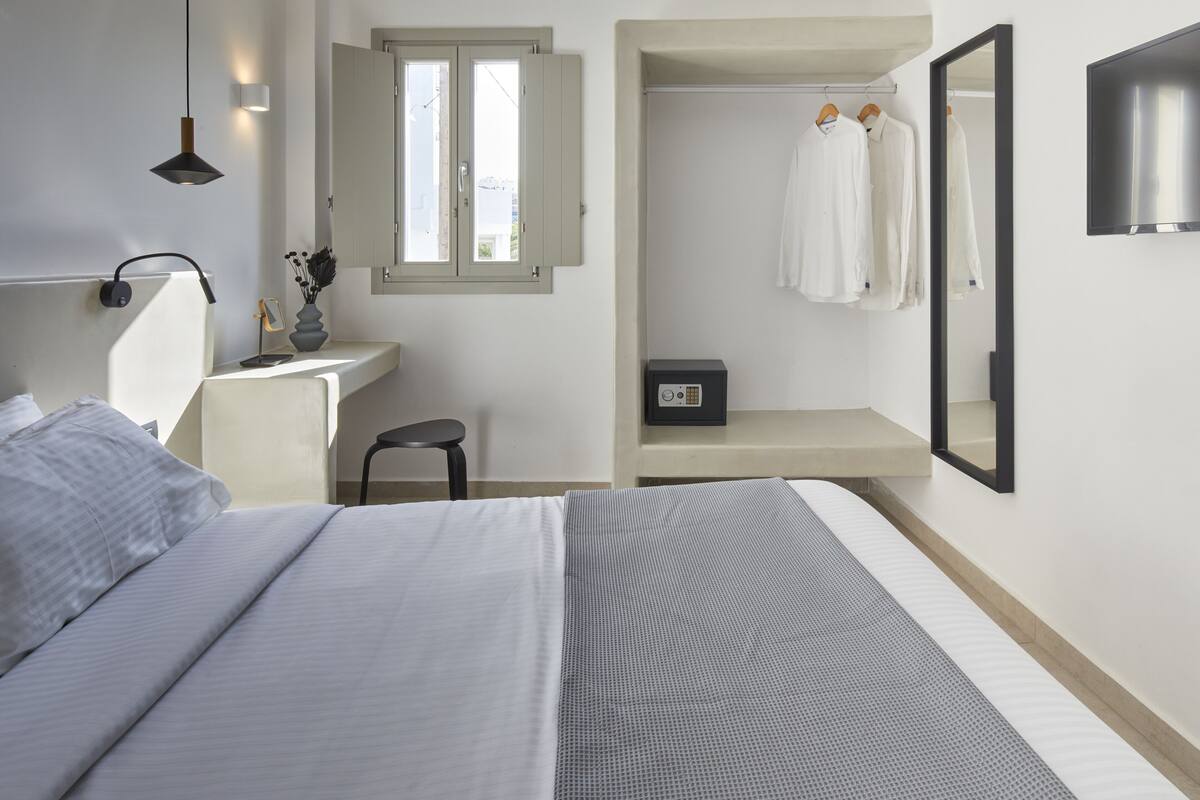 Een slaapkamer met een bed, nachtkastje, lamp, raam en een spiegel.