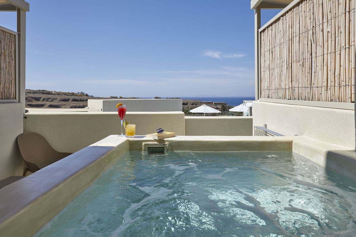 Een hottub met uitzicht op de oceaan, omgeven door een bamboomschutting en een witte parasol.
