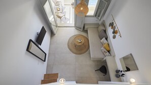 A modern interior with a sofa, a dining table, a hanging light fixture, and a view of the outdoors.