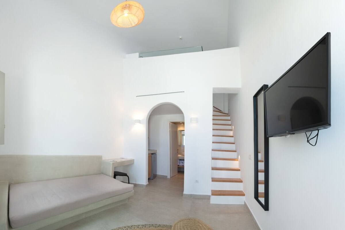 Een moderne woonkamer met een bank, een flatscreen-televisie aan de muur en een trap naar een andere kamer.