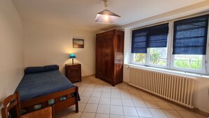 A bedroom with a bed, a nightstand with a lamp, a wardrobe, a window with blinds, and a radiator. - Renovated 4-Bedroom House near Loire Castles, Ideal for Families & Pros (Cléry-Saint-André)
