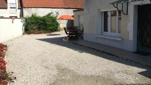 A residential property with a gravel driveway, a dining area with outdoor furniture, and a red umbrella. - Renovated 4-Bedroom House near Loire Castles, Ideal for Families & Pros (Cléry-Saint-André)