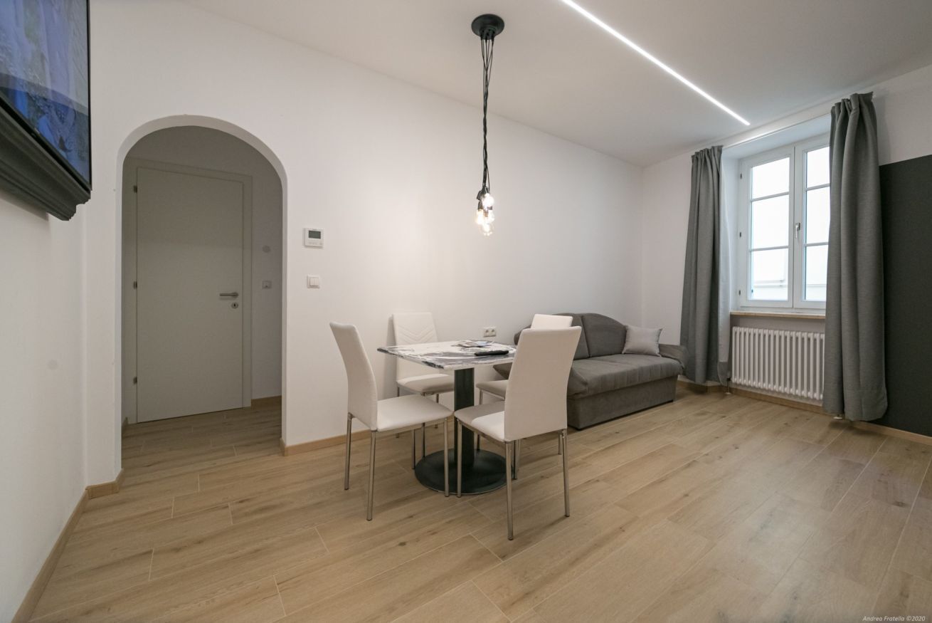 Een moderne woonkamer met een eetgedeelte, een bank en een aan de muur bevestigde televisie.