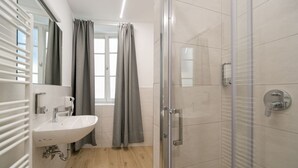Un bagno moderno con box doccia in vetro, lavandino bianco con specchio e finestra con tende.