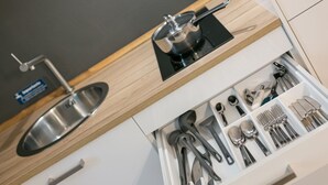 Una cucina con lavello in acciaio inossidabile, piano cottura e un cassetto pieno di utensili.