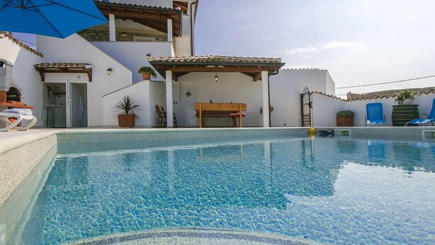 A poolside area with a clear pool, a wooden bench, and a pergola with a blue umbrella. - Holiday home with a pool for 7 persons only 6 km from beautiful beaches. (Porec)