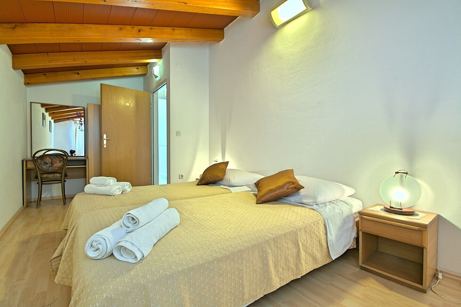 Ein Hotelzimmer mit zwei Betten, einem Holztisch, einem Stuhl und einer Nachttischlampe.