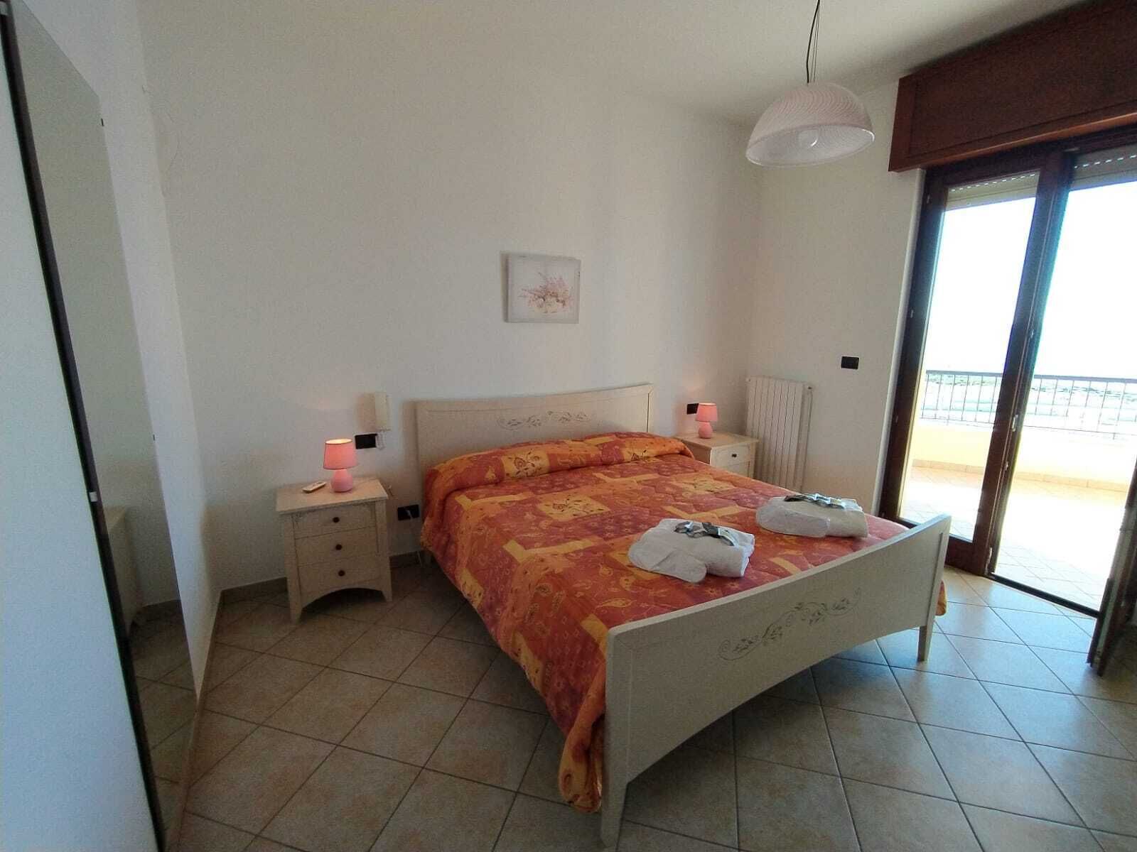 A bedroom with a bed, two bedside tables, a nightstand, a window, and a door.