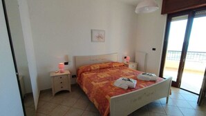 A bedroom with a bed, two bedside tables, a nightstand, a window, and a door. - Rosa Virginia vista mare (Gallipoli)