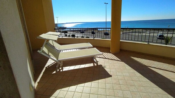 A balcony with two sun loungers, a tiled floor, and a view of the sea and parking area. - Rosa Virginia vista mare (Gallipoli)