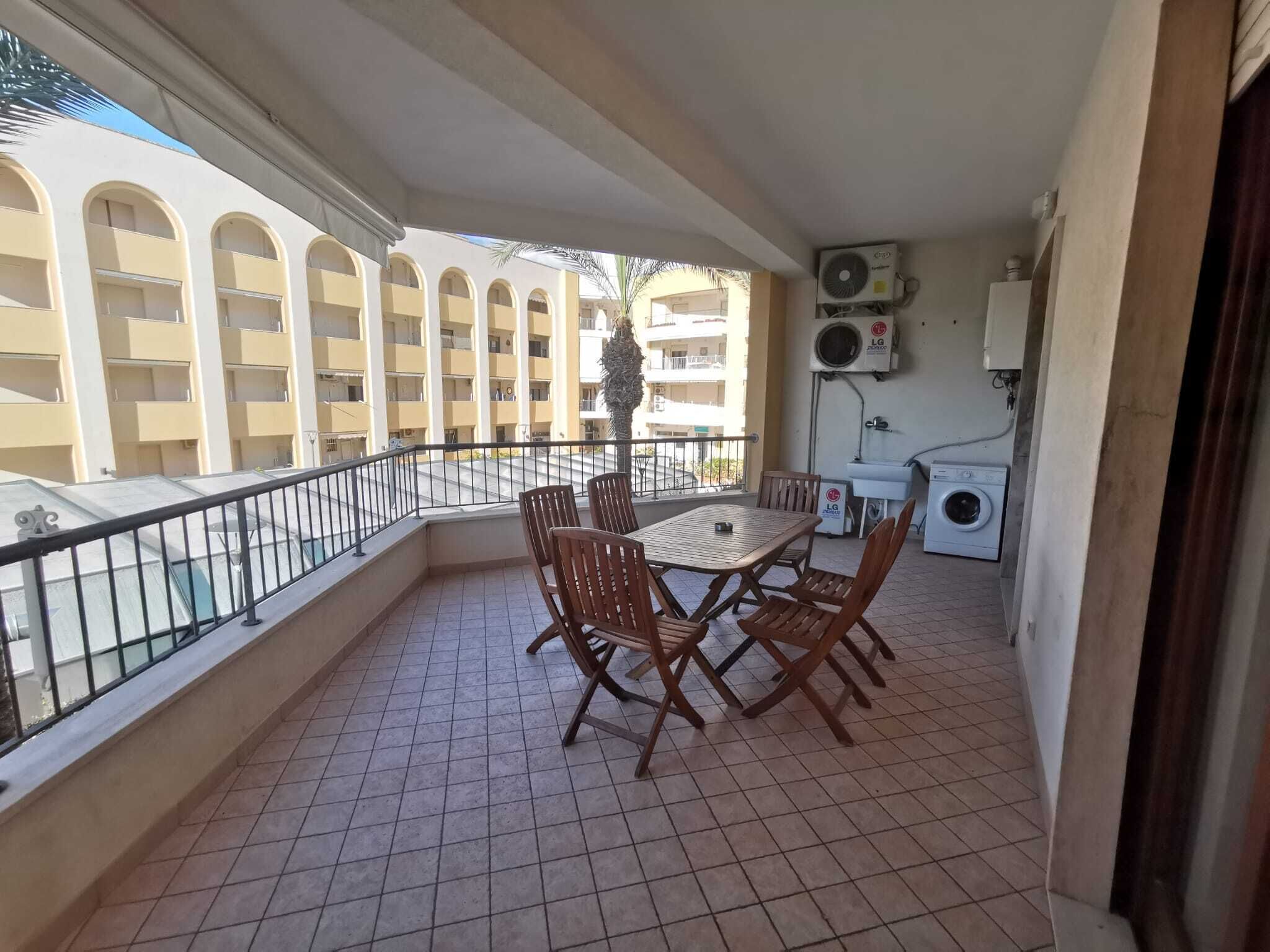 A balcony with a table and chairs, a washing machine, and an air conditioning unit.