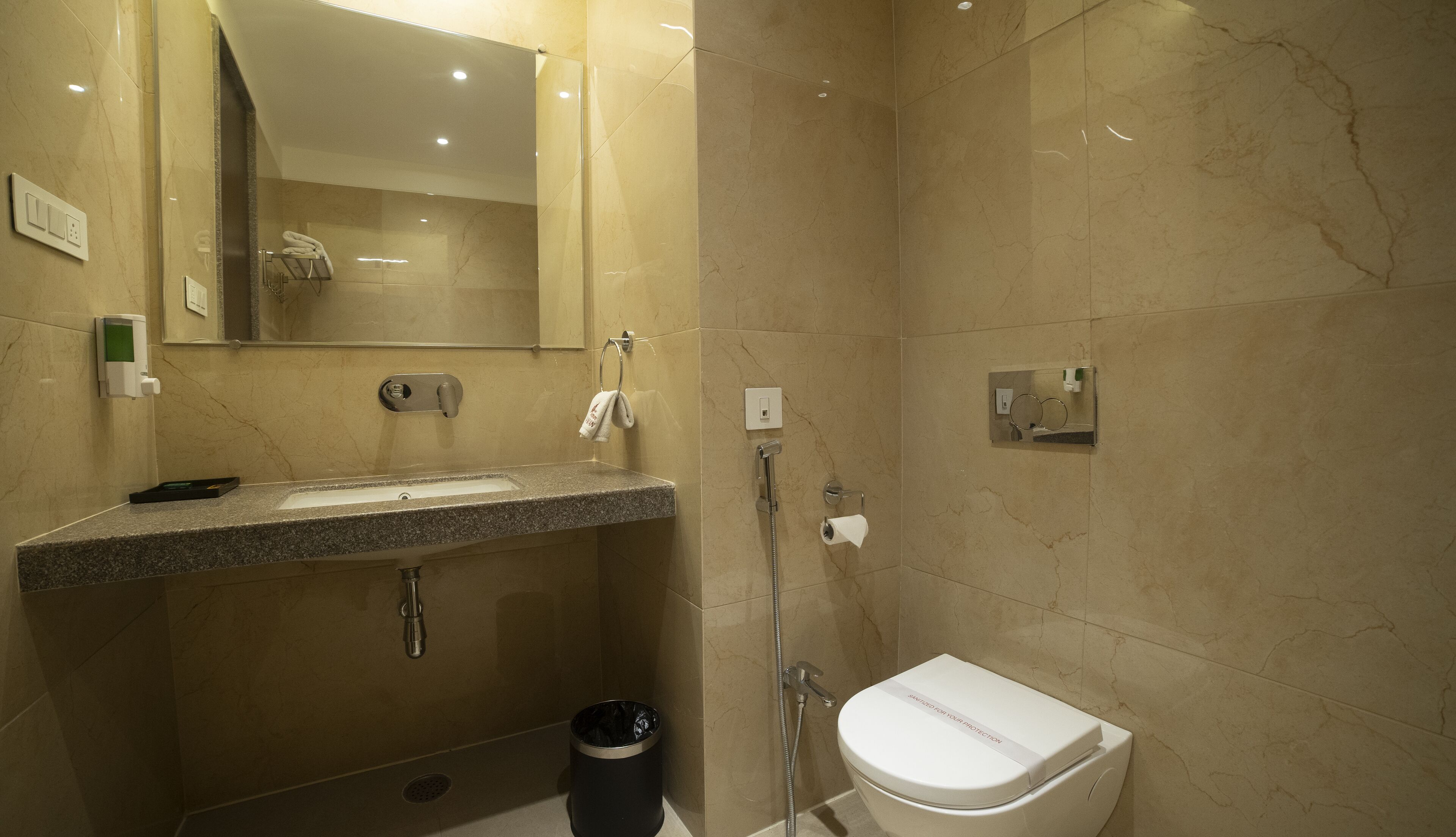 Une salle de bain moderne avec un lavabo doté d’un plan de travail en granit, un miroir, une douchette à main et des toilettes.