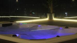 A heated outdoor pool with a curved edge and a potted plant nearby. - Hotel Rajhans Abhinandan (Bhopal)
