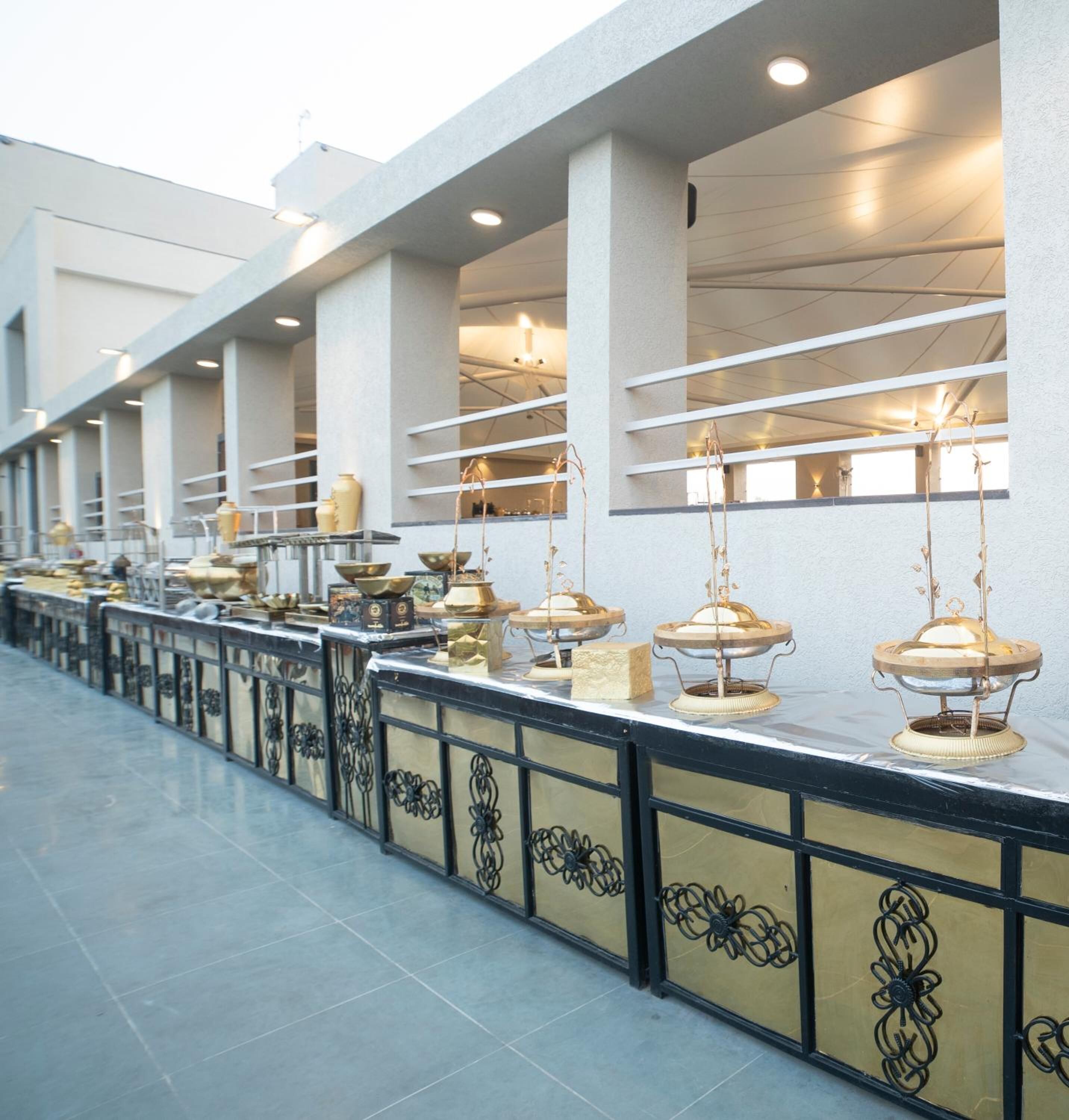 A long, covered outdoor seating area with tables and chairs, a railing with decorative patterns, and overhead lighting.