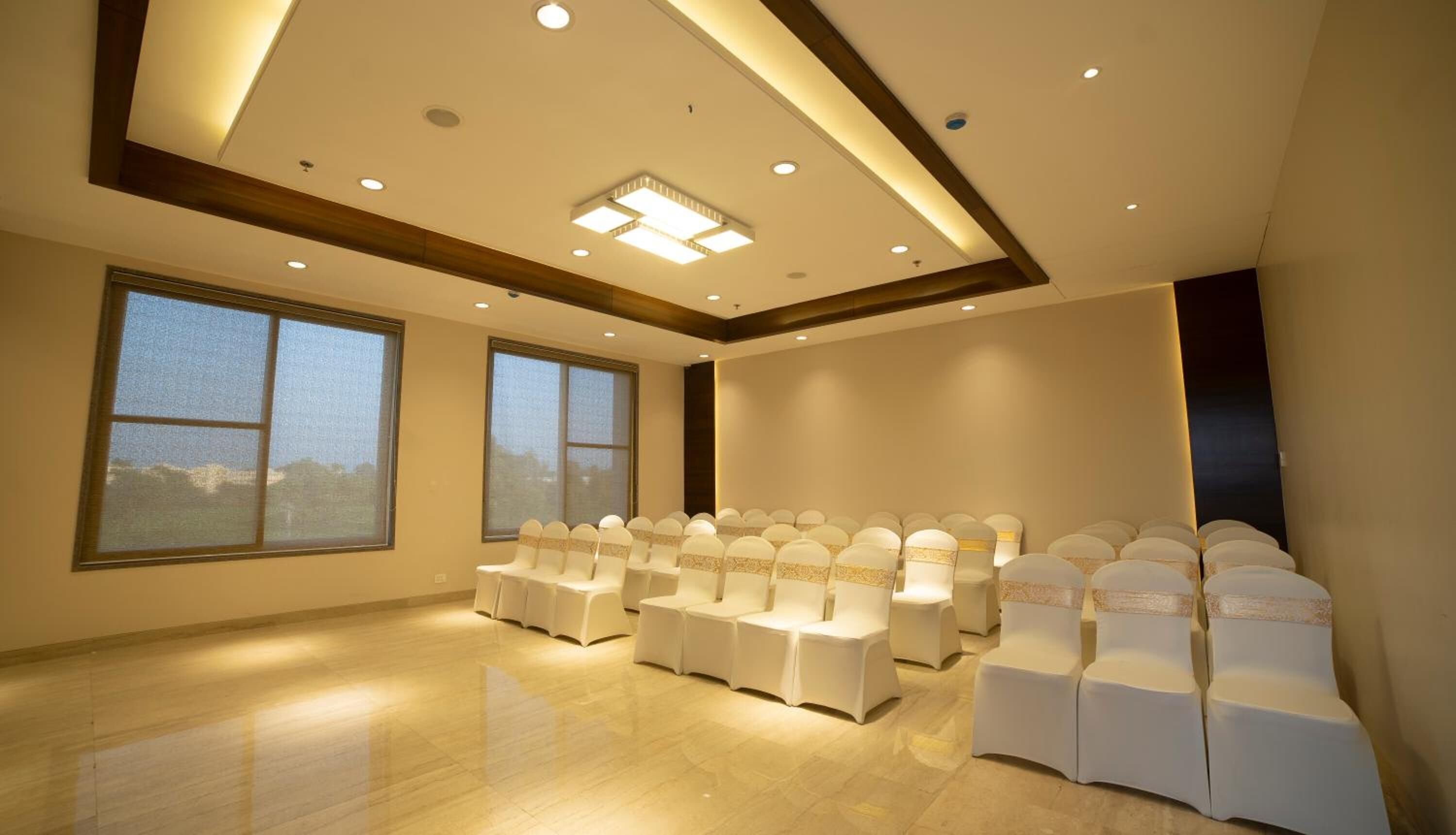 Un salón de conferencias con filas de sillas blancas, ventanas amplias y un diseño moderno en el techo.