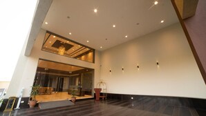 A spacious lobby with a high ceiling, recessed lighting, and a modern chandelier. There is a reception desk with a cart and potted plants. - Hotel Rajhans Abhinandan (Bhopal)