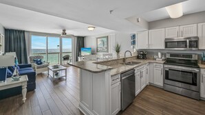 Eine moderne Küche mit weißen Schränken, einer großen Kochinsel mit Spüle und einem eingebauten Backofen. Es gibt einen Balkon mit Meerblick.