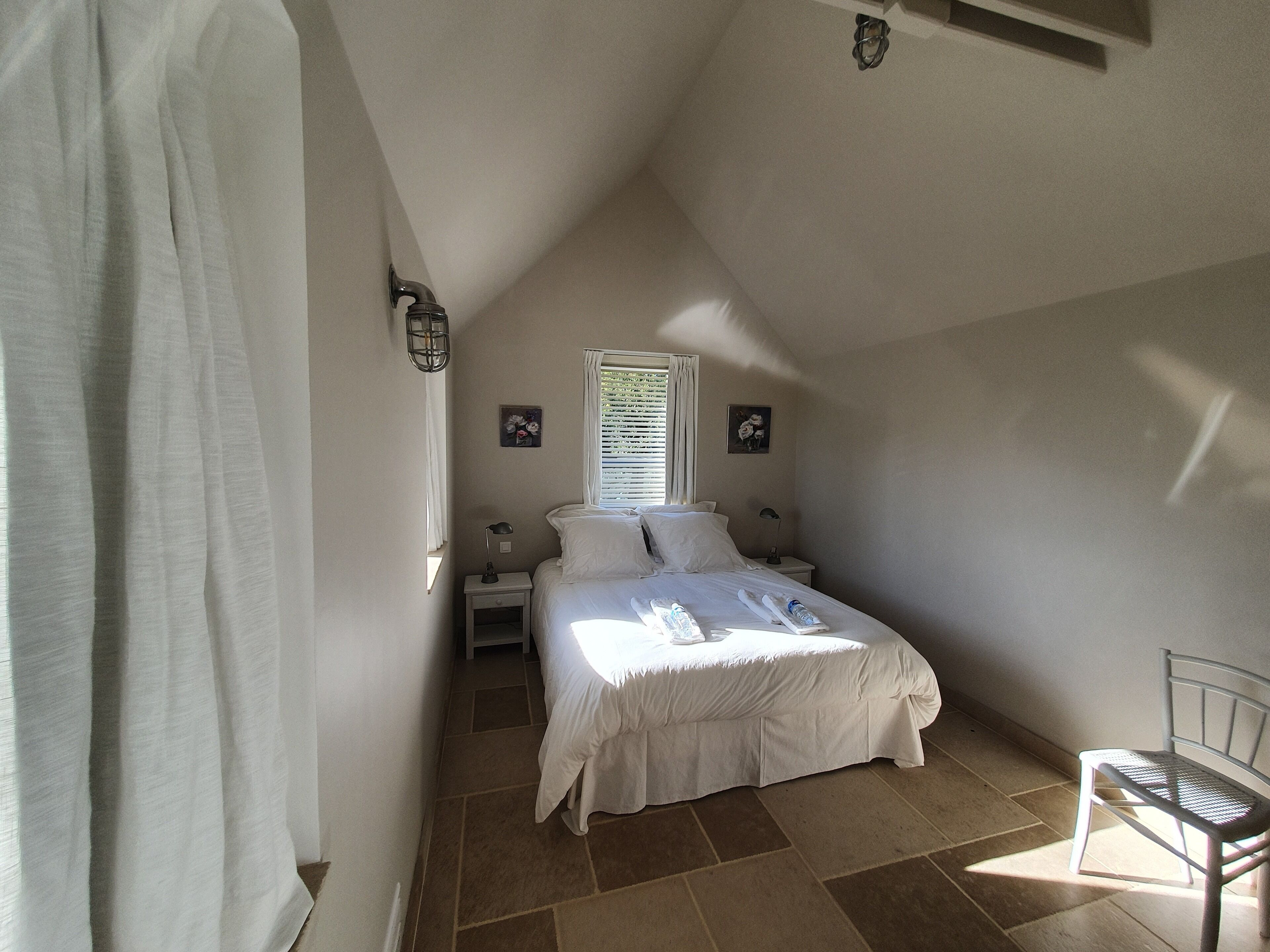 A bedroom with a bed, a nightstand, a chair, and a window with blinds.
