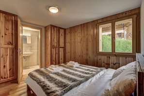 Quarto de madeira com uma cama, janela e banheiro.