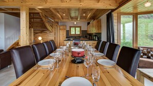 Un tavolo da pranzo in legno apparecchiato per sei persone, sedie, una cucina sullo sfondo e vista sul verde all'esterno.