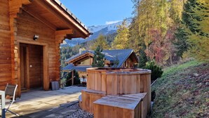 Una baita in legno con idromassaggio e vista su una catena montuosa boscosa.