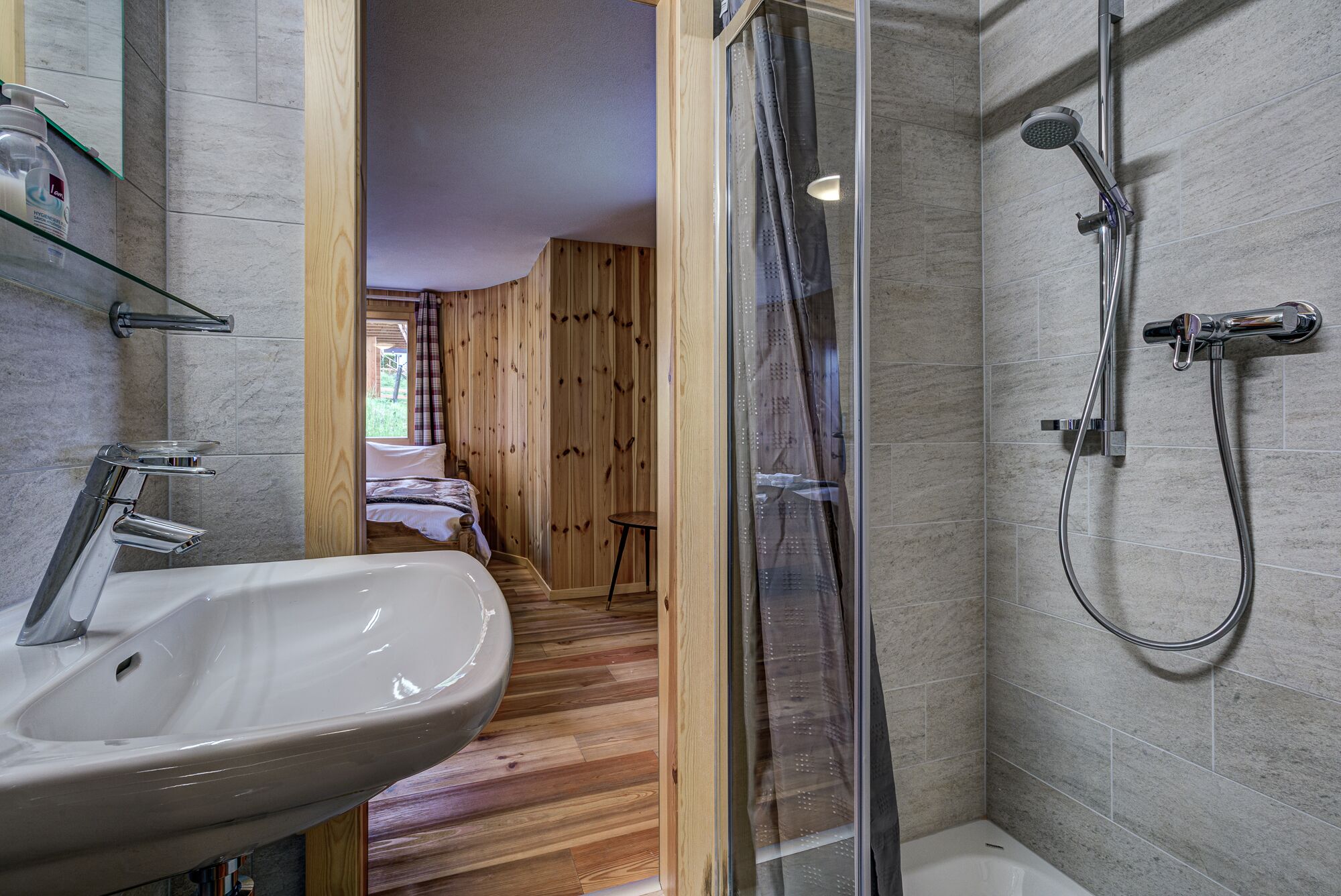 Ein Badezimmer mit einem weißen Waschbecken, einer Dusche mit Duschbrause und einer gläsernen Duschkabine.