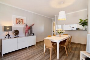 A modern dining area with a white table and chairs, a pendant light, and a white cabinet with decorative items.