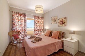 A bedroom with a bed, a nightstand, a chair, and a window with curtains.