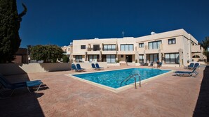 A swimming pool with lounge chairs and a building with multiple balconies in the background. - Apt. Suri, Modern 2BDR Apt. in the heart of Ayia Napa, Close to Nissi Avenue (Ayia Napa)