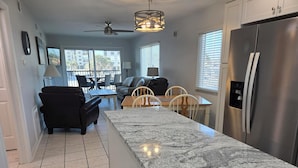 A modern kitchen with a granite countertop, stainless steel refrigerator, and a dining area with a table and chairs. - Estero Sands Condo with 2 bedrooms and 2 baths (Fort Myers Beach)
