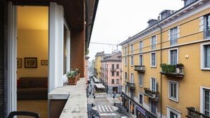 Une rue étroite bordée d’immeubles jaunes, un balcon avec une chaise, et un passage piéton.