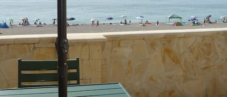 A beach view with a stone wall, a green table, and a metal chair.