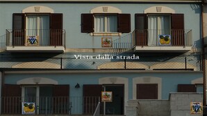 A multi-story building with balconies, some with shutters, and signs indicating 'UVA' and 'Limoncello'. - GALATEA - One step away from the sea - LEMON. (Mascali)