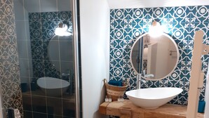Un baño con cabina de ducha de vidrio, un lavamanos blanco con espejo y azulejos decorativos en las paredes.