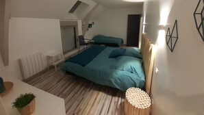 Un dormitorio con techo inclinado, una cama con ropa de cama azul, una mesita con una planta y un aplique de pared.