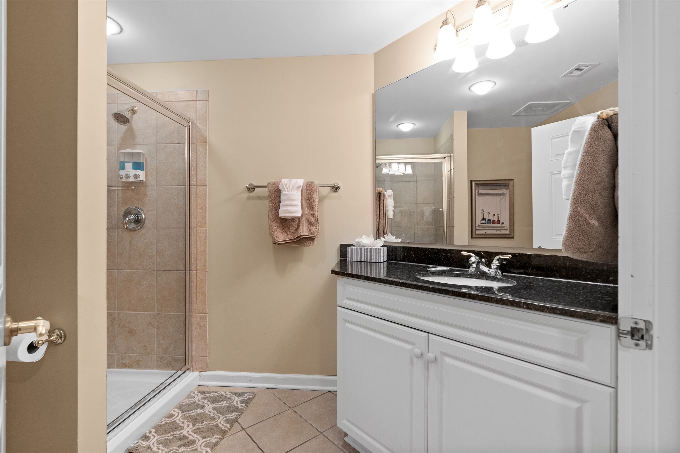 A bathroom with a glass shower enclosure, a sink with a vanity, and a mirror.