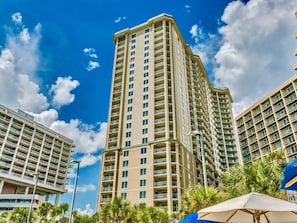 Un hotel moderno con numerosi balconi, un cielo azzurro e palme sullo sfondo.
