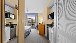 A narrow hotel room with a kitchenette, a bed, a desk, and a view of the outside. - Royale Palms 1201H Oceanview Studio in Kingston (Myrtle Beach)