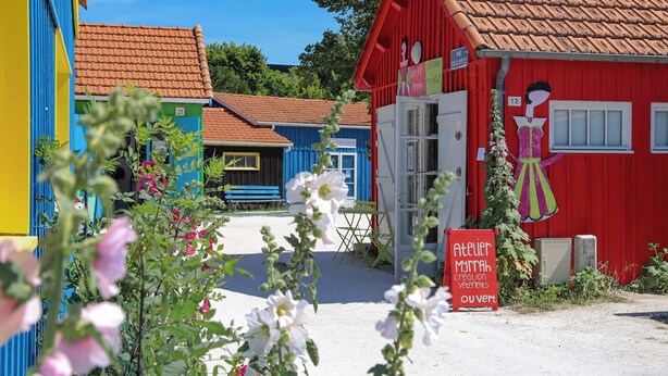 A colorful building with a red facade and a blue door, a bench, and a sign indicating a workshop. - Vacation home 3* LES MATHES/LA PALMYRE (Les Mathes)