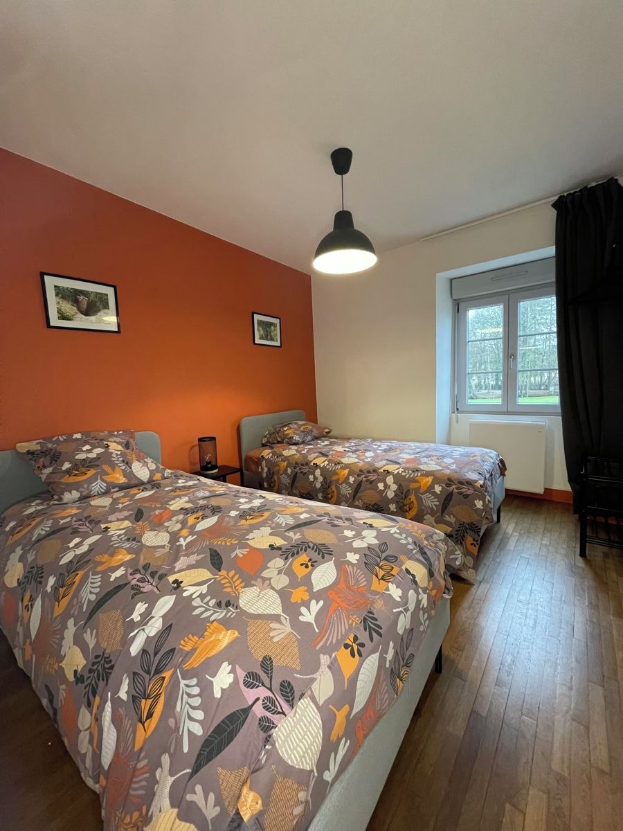 A room with two beds, a window with curtains, a ceiling light, and two framed pictures on the wall.