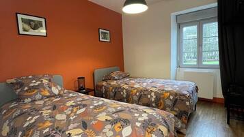 A room with two beds, a window with curtains, a ceiling light, and two framed pictures on the wall.