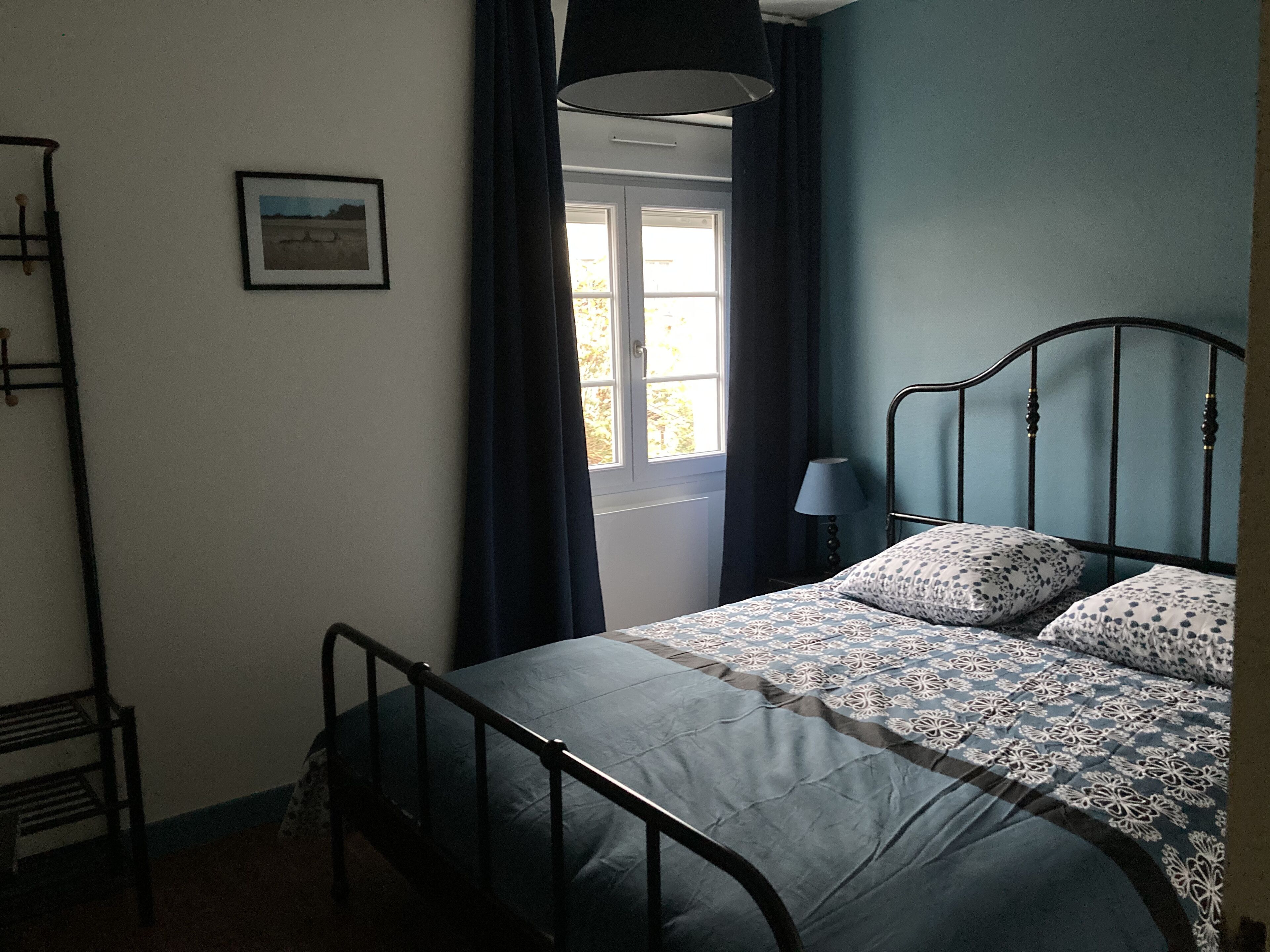 A bedroom with a bed, a window with curtains, a bedside lamp, and a picture on the wall.