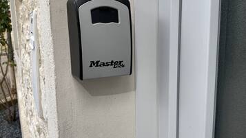 Un cadenas de la marque Master Lock est fixé sur un mur beige, près d’une porte blanche.