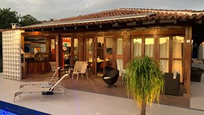 A covered outdoor seating area with chairs and a table, a pool, and a potted plant.