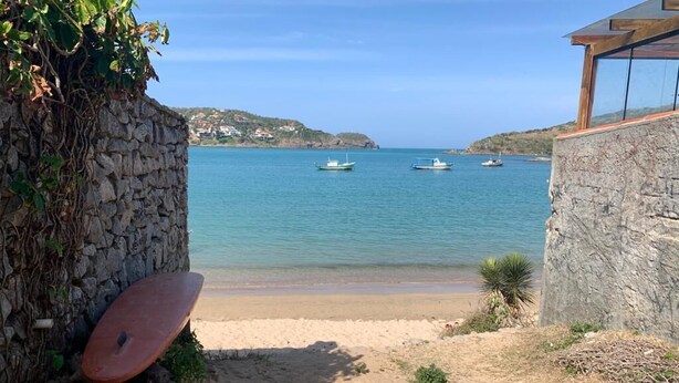 A beach with a stone wall, a surfboard, and boats on the water.