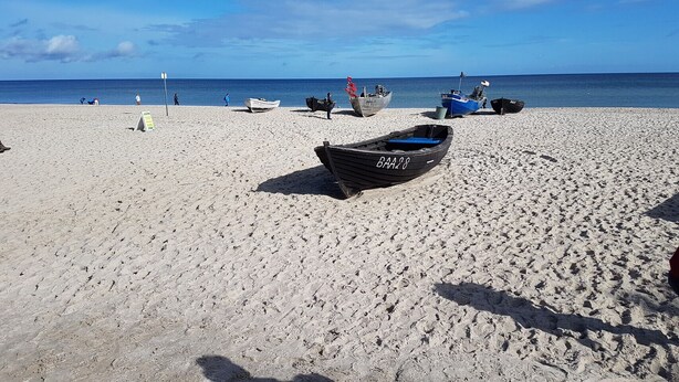 Uma praia arenosa com vários barcos e algumas pessoas.