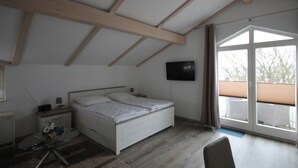 Quarto com cama, televisão na parede e uma grande janela com persianas.