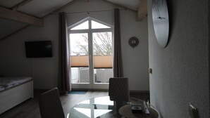 Um quarto com cama, cadeira, mesa, relógio e uma janela grande.